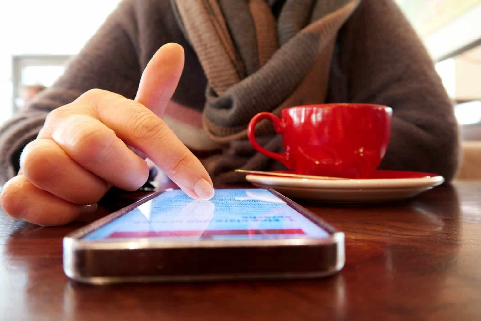 Person using a smartphone with a cup of coffee.