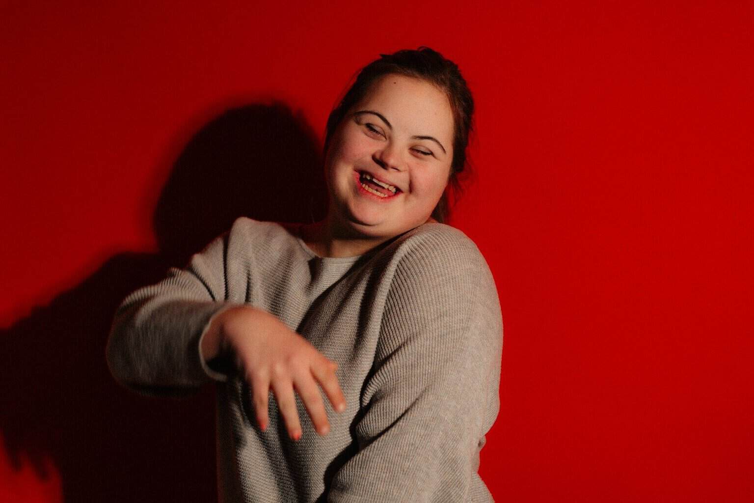 A young woman with down syndrome laughs against red background